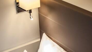 Habitación de hotel con cabecera, lámpara de noche y dos almohadas.