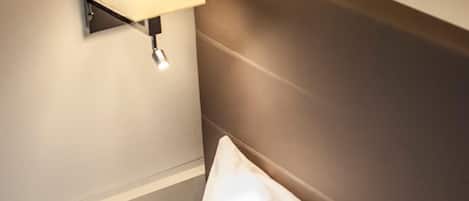 Habitación de hotel con cabecera, lámpara de noche y dos almohadas.