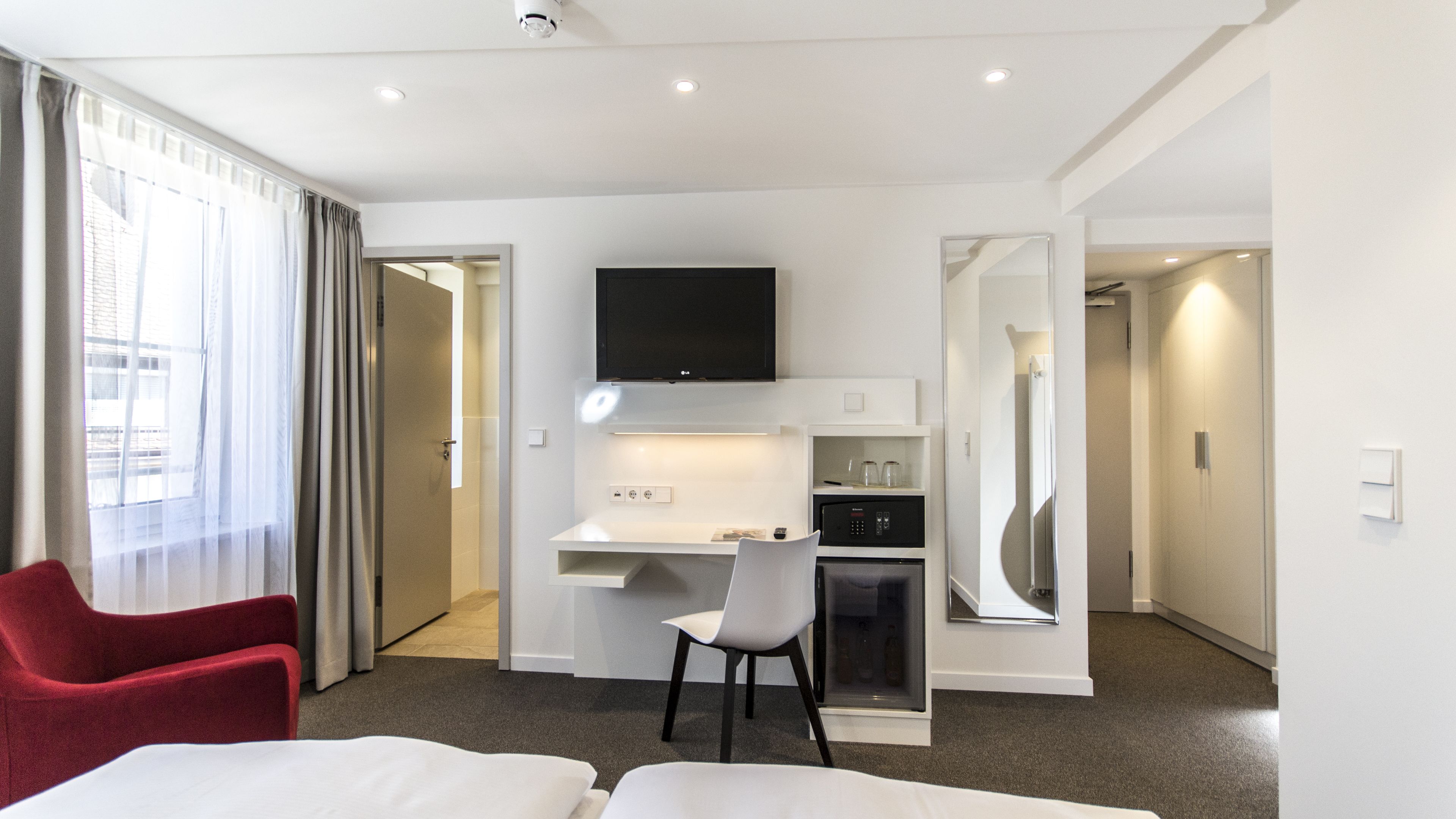 Una habitación de hotel con cama, escritorio, silla, televisión y minibar.