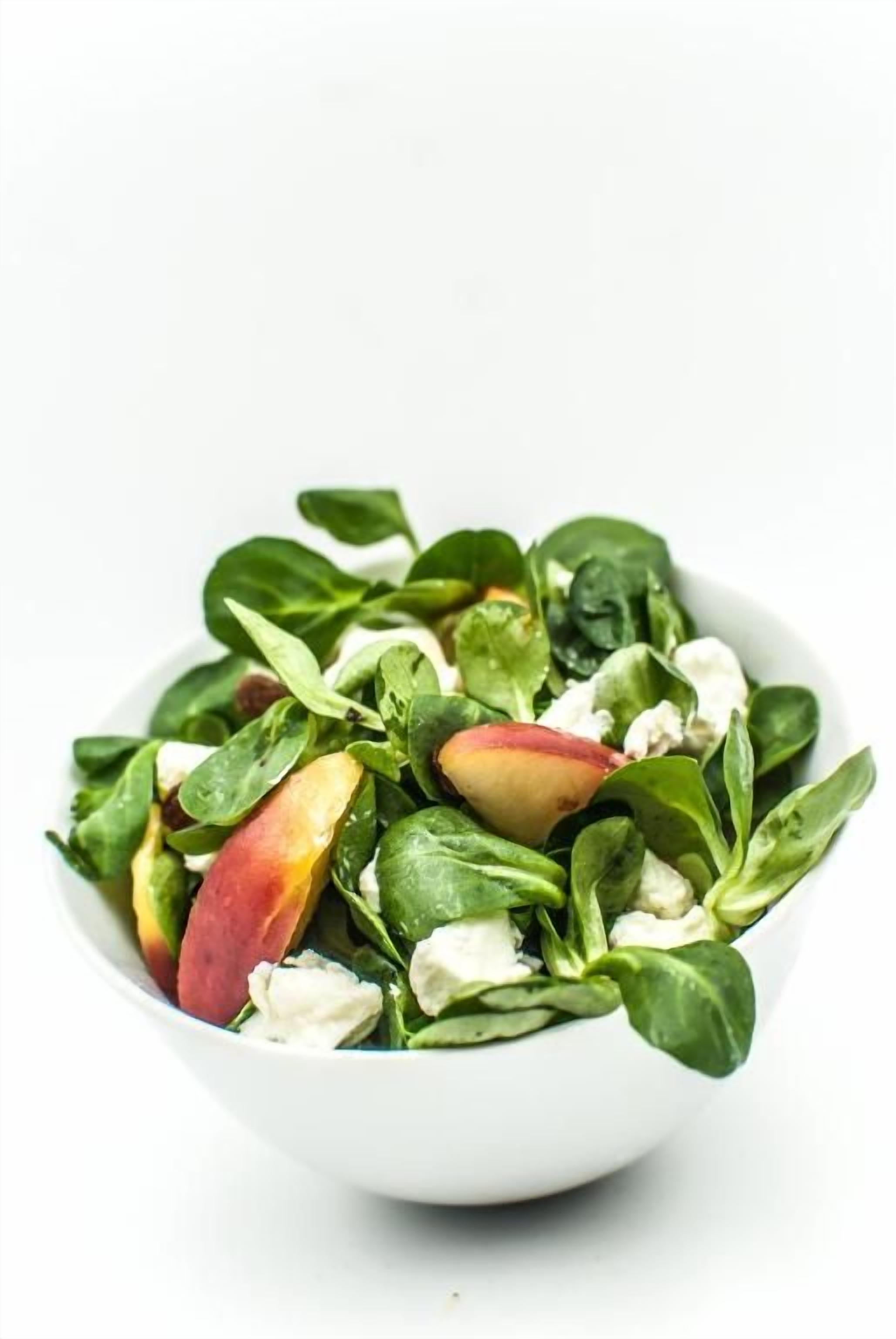 Un tazón blanco con una ensalada de hojas verdes y trozos de fruta roja.
