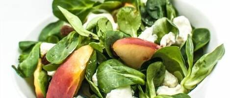Un tazón blanco con una ensalada de hojas verdes y trozos de fruta roja.