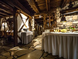 Interior rústico com paredes de pedra, vigas de madeira e mesas preparadas para refeições.