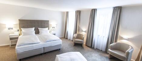 A hotel room with a large bed, two bedside tables, a chair, and a desk.