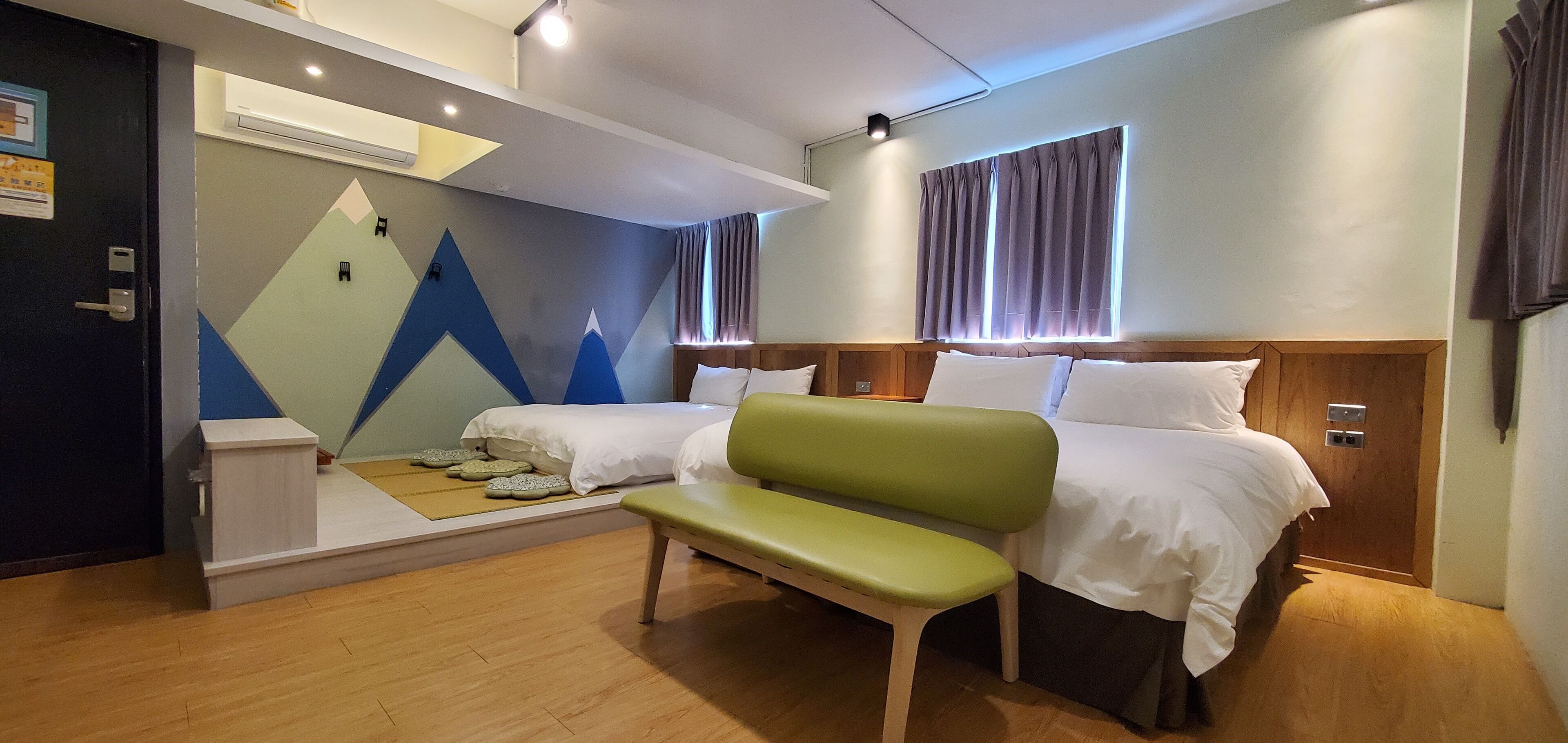 A hotel room with two beds, a bench, a geometric wall design, and a window with curtains.