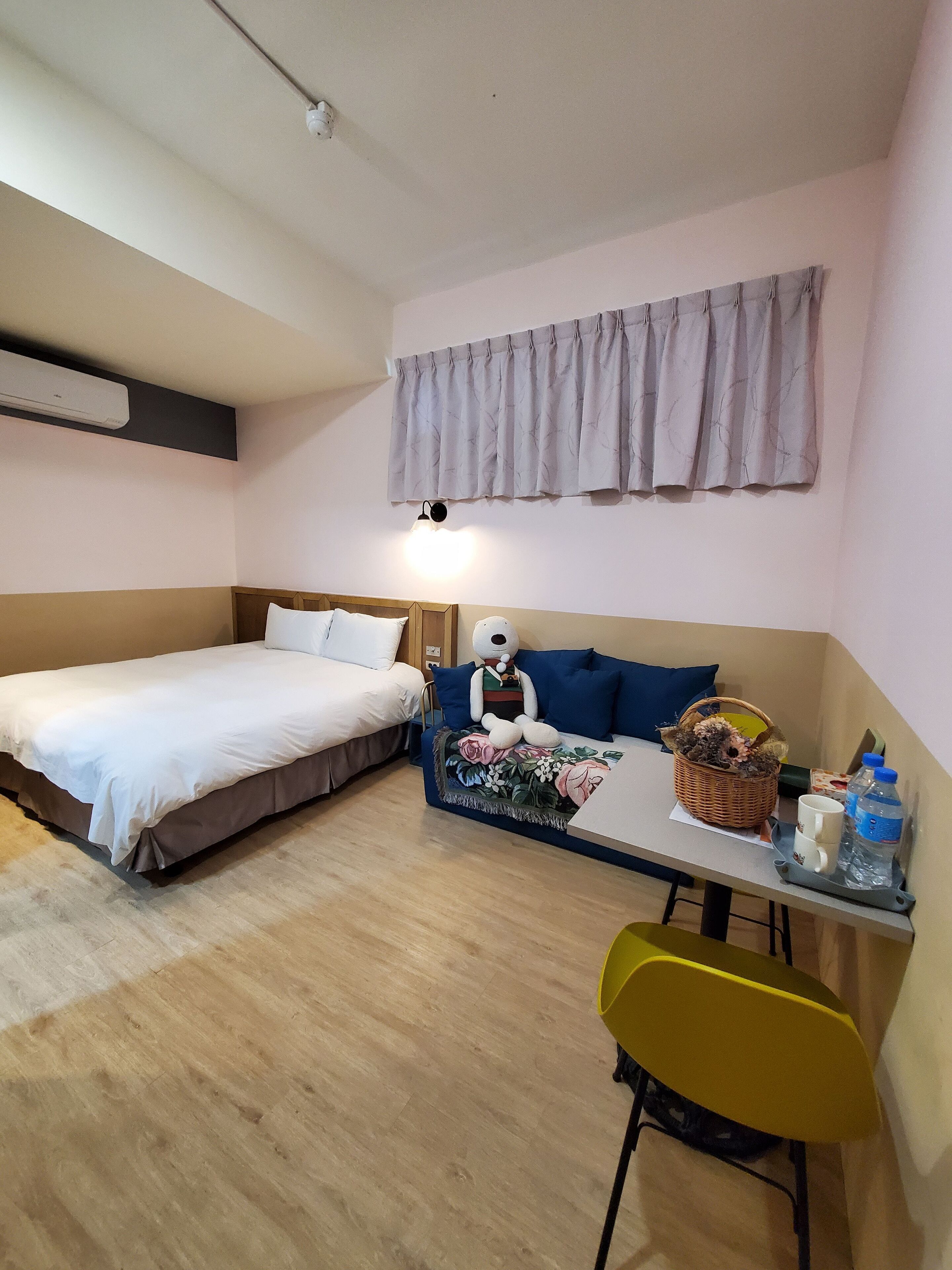 Habitación de hotel con dos camas, un sofá, una mesa con una cesta, una botella de agua y una silla.