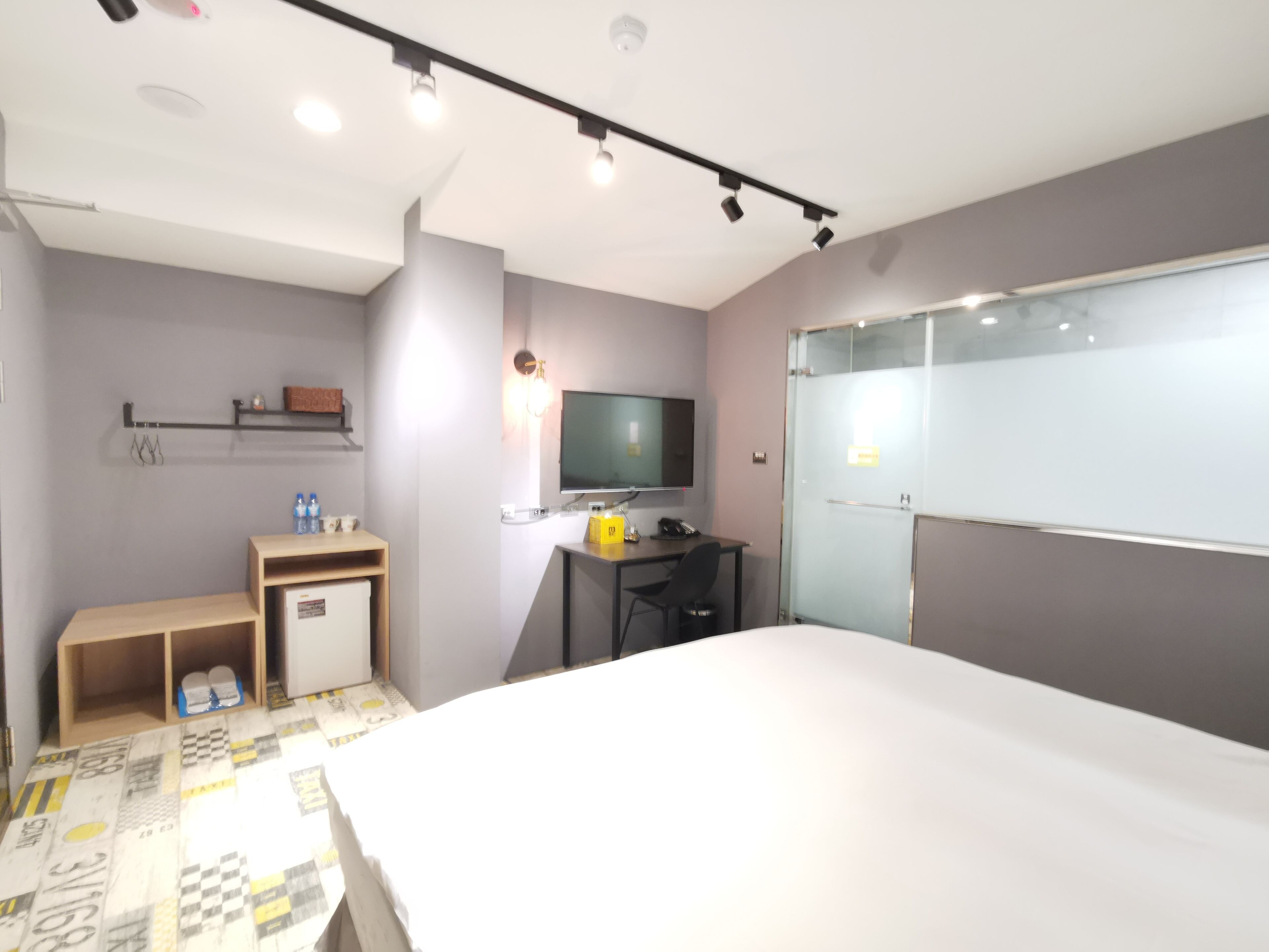 Habitación de hotel moderna con cama, escritorio, silla, televisor y un pequeño estante con artículos de aseo.
