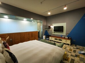 Habitación de hotel con una cama grande, un tocador con espejo, un televisor montado en la pared y una alfombra estampada en el suelo.