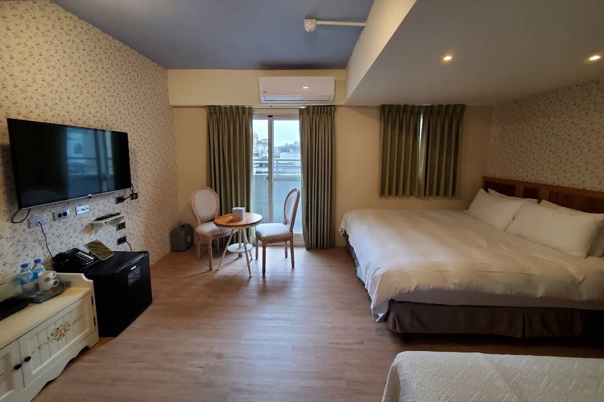 Quarto de hotel com cama, televisão, mesa pequena com cadeiras, máquina de café e vista para a cidade pela janela.