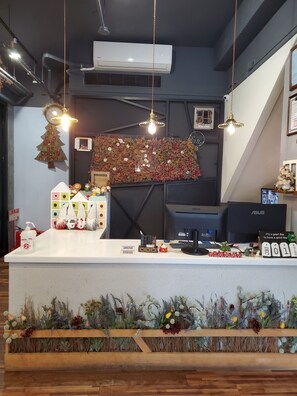 Una zona de recepción con mostrador blanco, figuras decorativas de gnomos, decoración navideña en forma de árbol y un reloj.