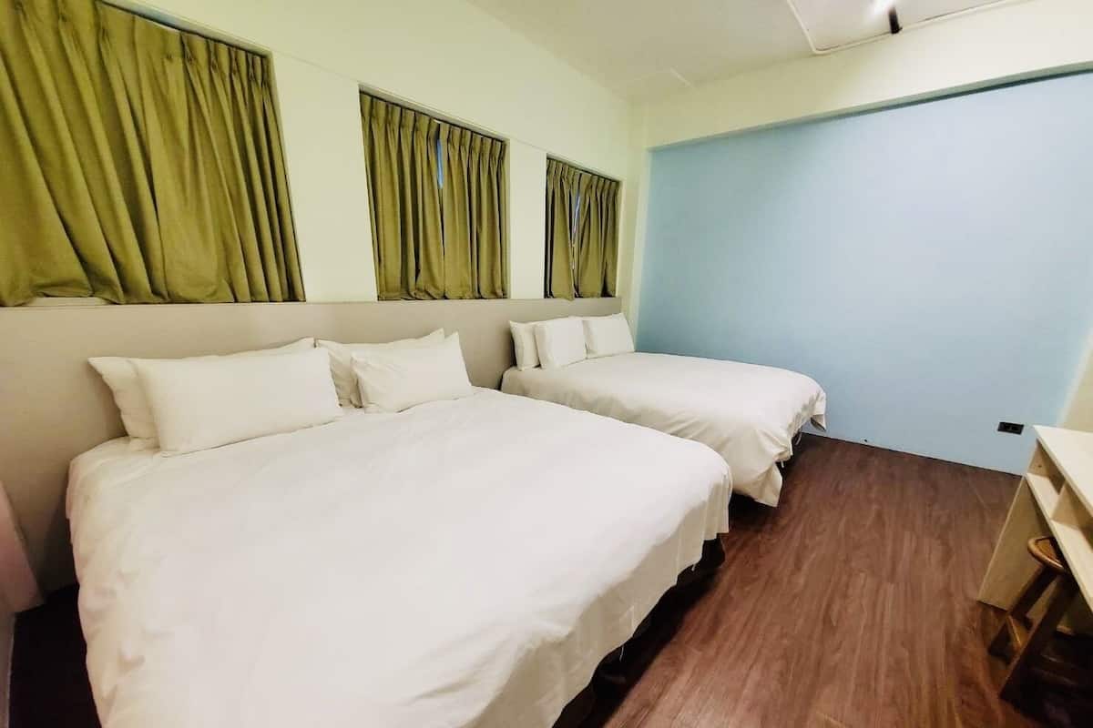 Quarto de hotel com duas camas, uma mesa e parede azul claro.