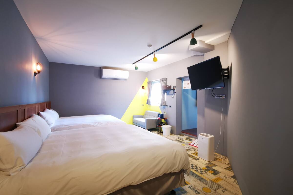 Quarto de hotel com cama, escrivaninha, cadeira, televisão e janela com cortinas.