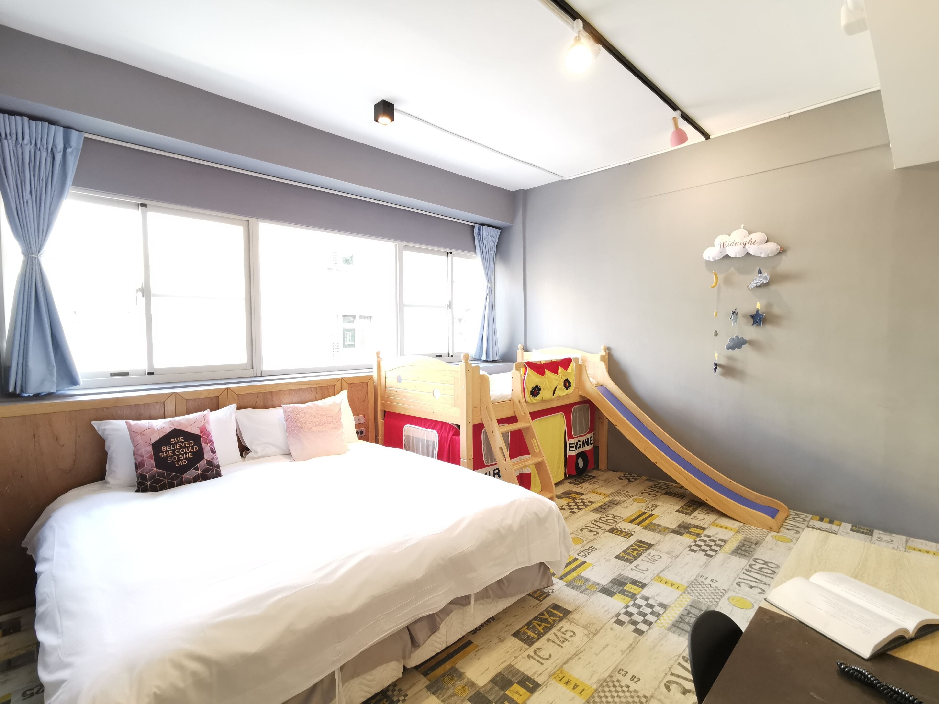 Un dormitorio con cama, un escritorio pequeño, una ventana con cortinas, una litera y una decoración en la pared.