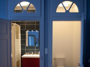Un baño con inodoro blanco, tocador rojo y espejo sobre el lavabo.