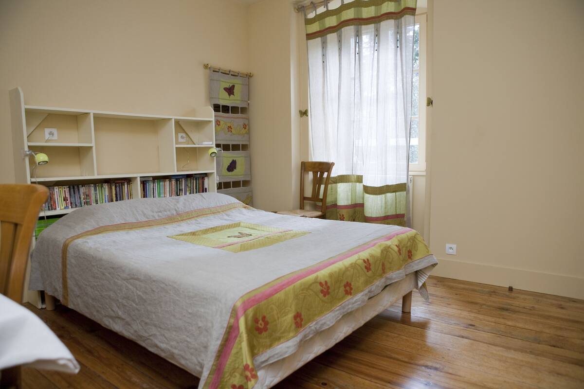 Un dormitorio ordenado con cama, una estantería y una ventana con cortinas.