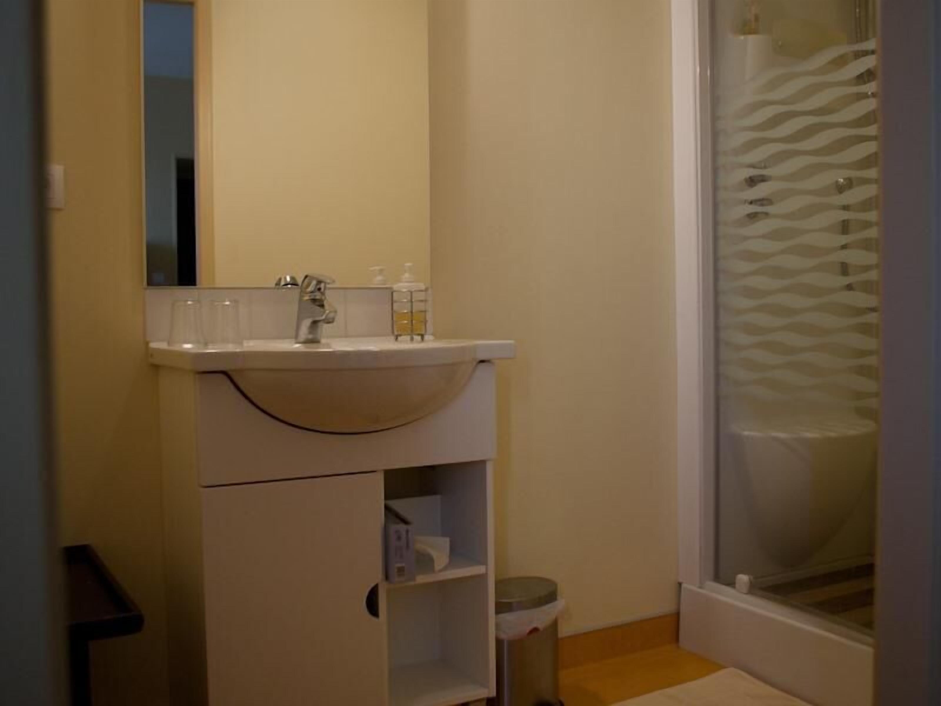 A bathroom with a white sink, mirror, and a shower with a wavy glass door.