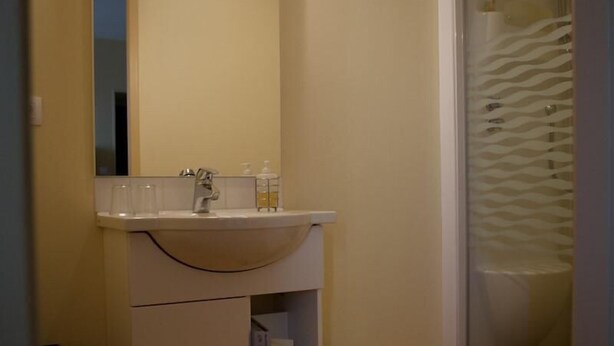 A bathroom with a white sink, mirror, and a shower with a wavy glass door. - Le Relais du Passe-Heures (Cenans)