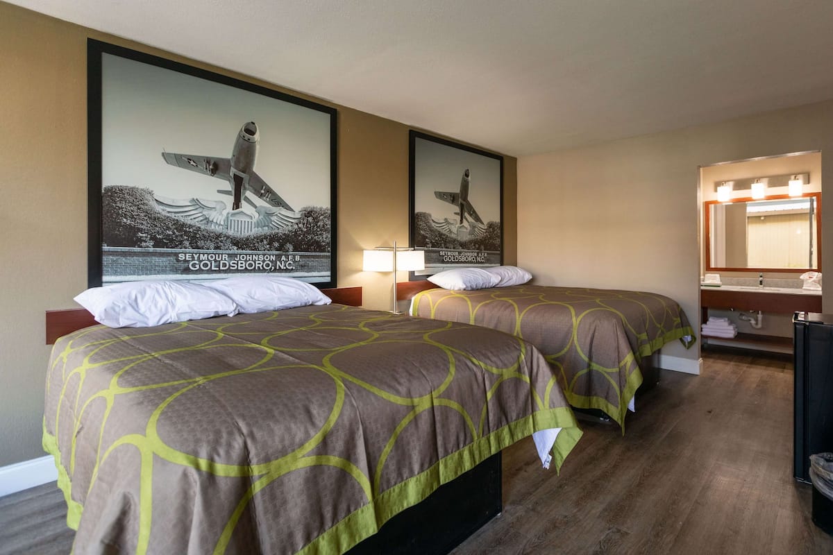 Habitació d'hotel amb dos llits, un mirall gran i una fotografia amb marc d'un surfista sobre una onada.
