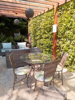 An outdoor patio with wicker furniture and a glass table, surrounded by a wall of climbing plants. - Pousada do Cardoso (Angra dos Reis)