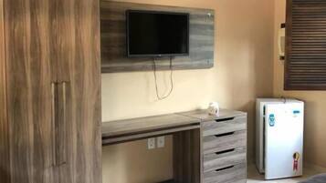 Una habitación con armario, escritorio con cajones, televisor montado en la pared, refrigerador y dos camas.