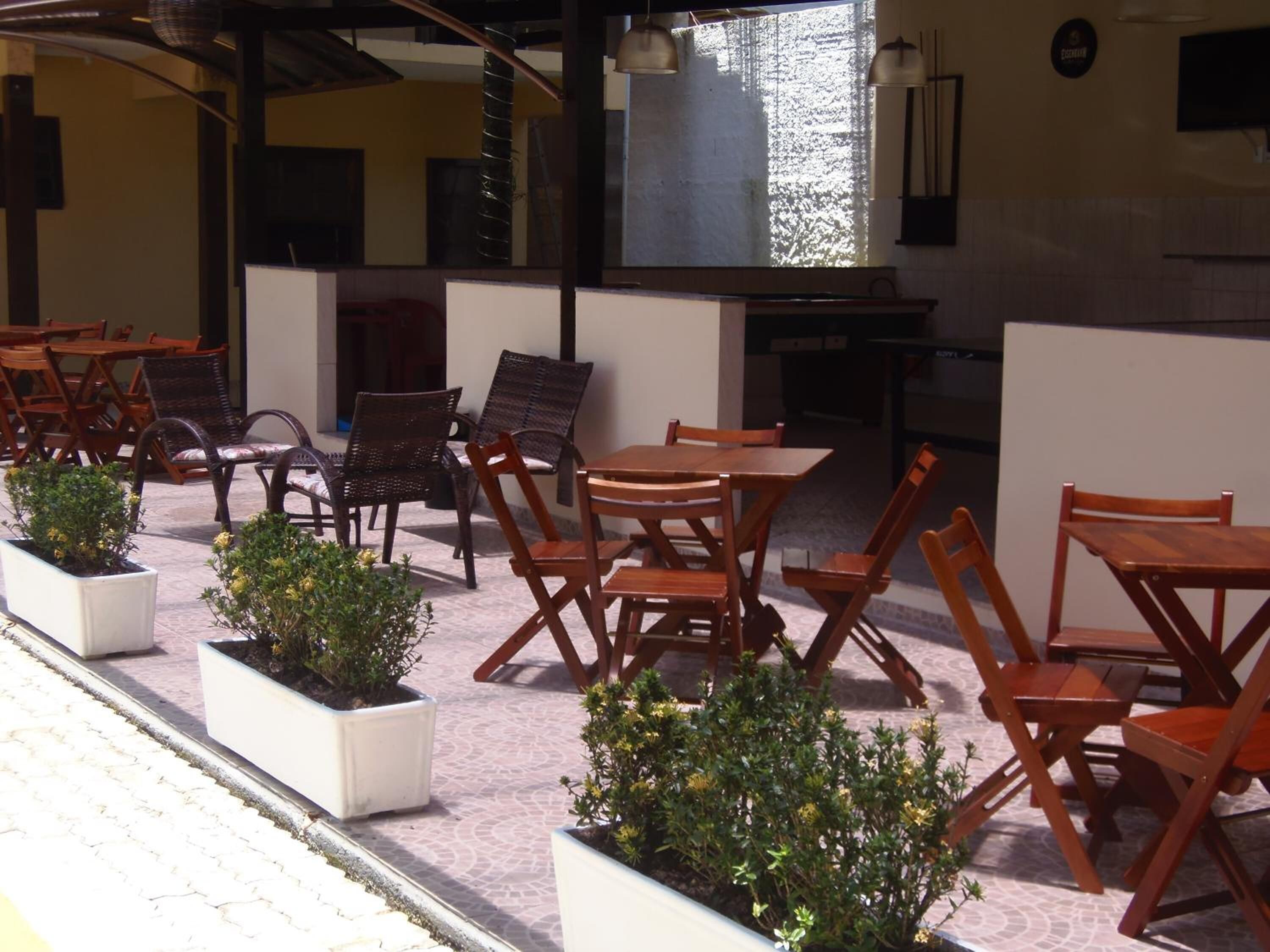 An outdoor patio with wooden tables and chairs, potted plants, and a view of the interior.