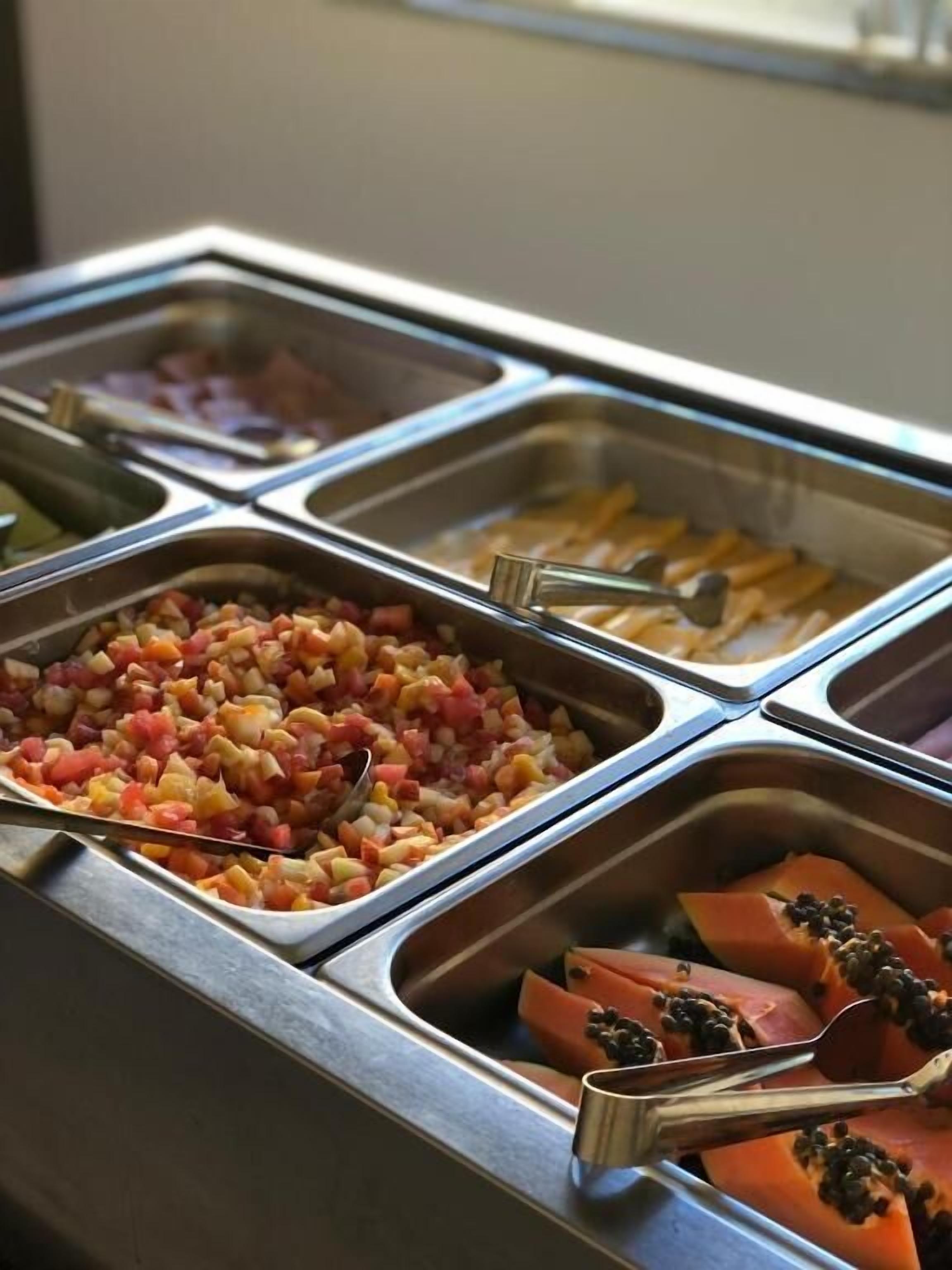 Un bufé con diversas opciones de comida en recipientes de metal.