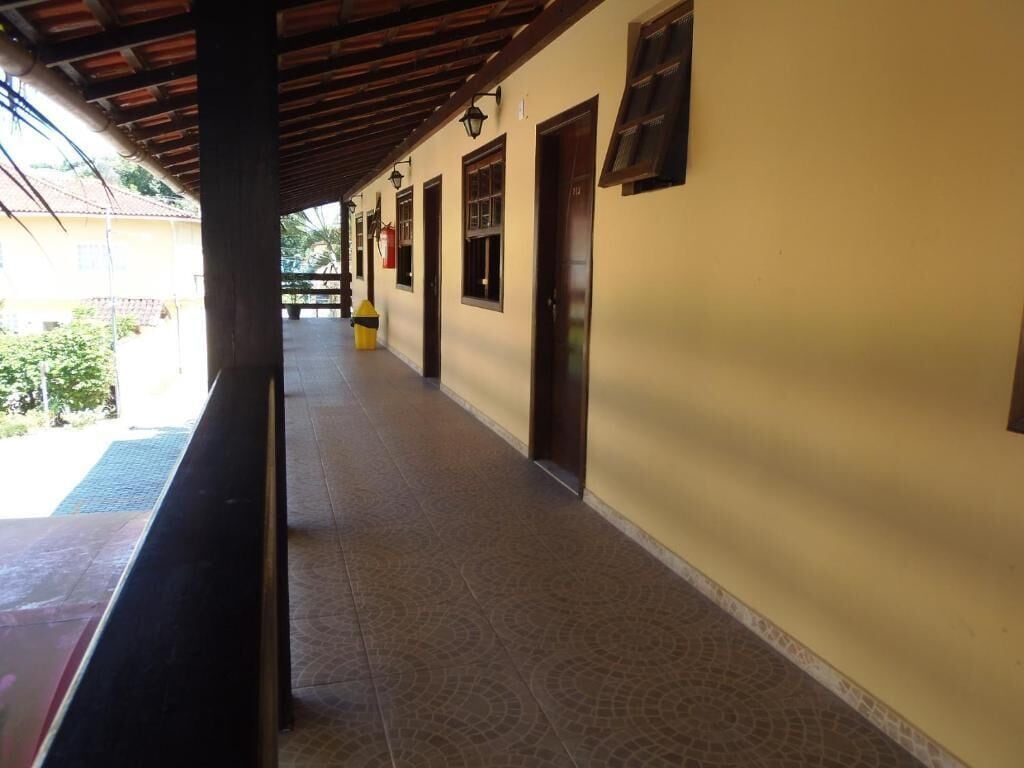 A covered corridor with tiled flooring, wooden beams, and doors leading to rooms.
