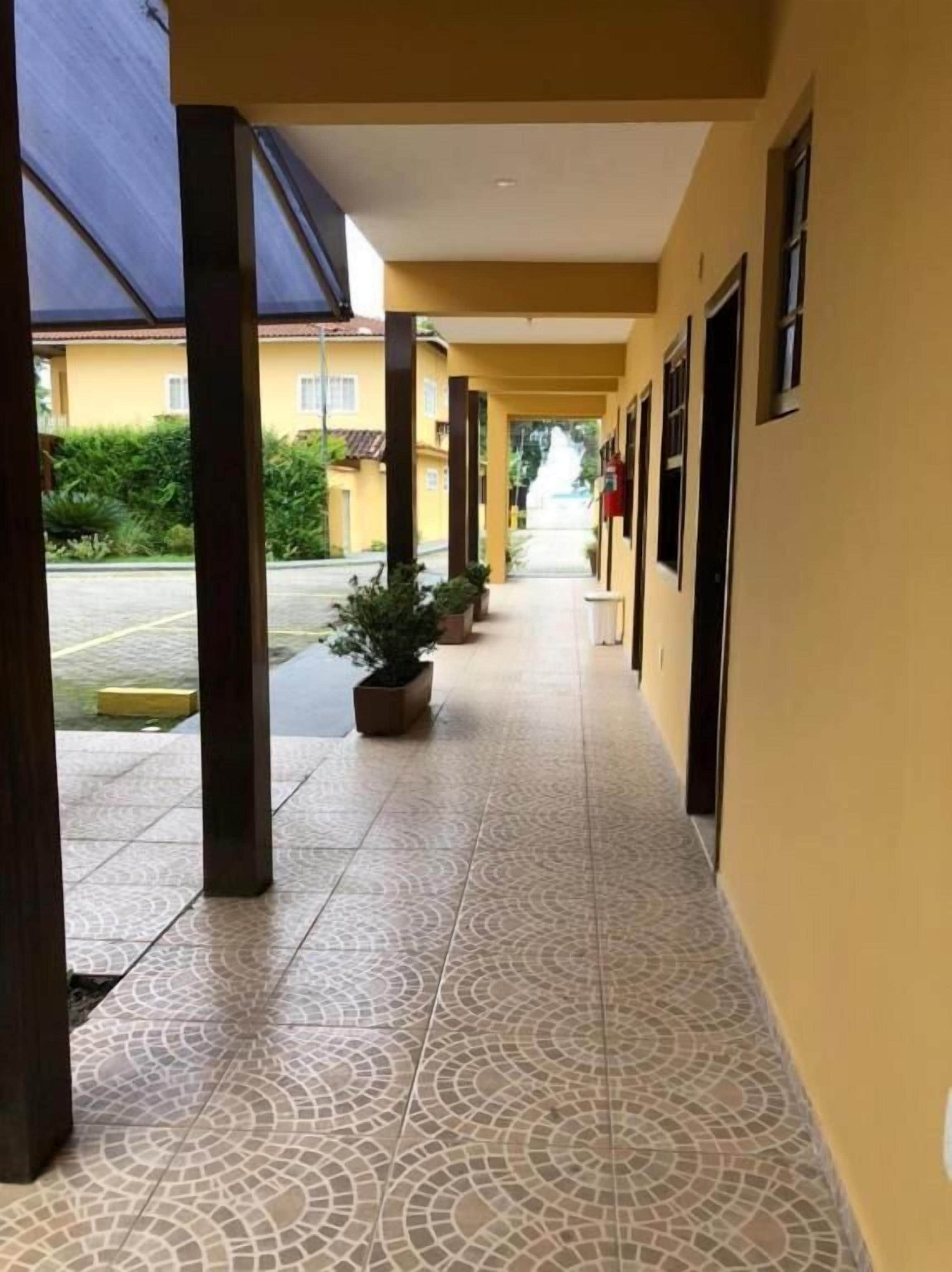 A corridor with tiled flooring, potted plants, and a row of doors on one side.