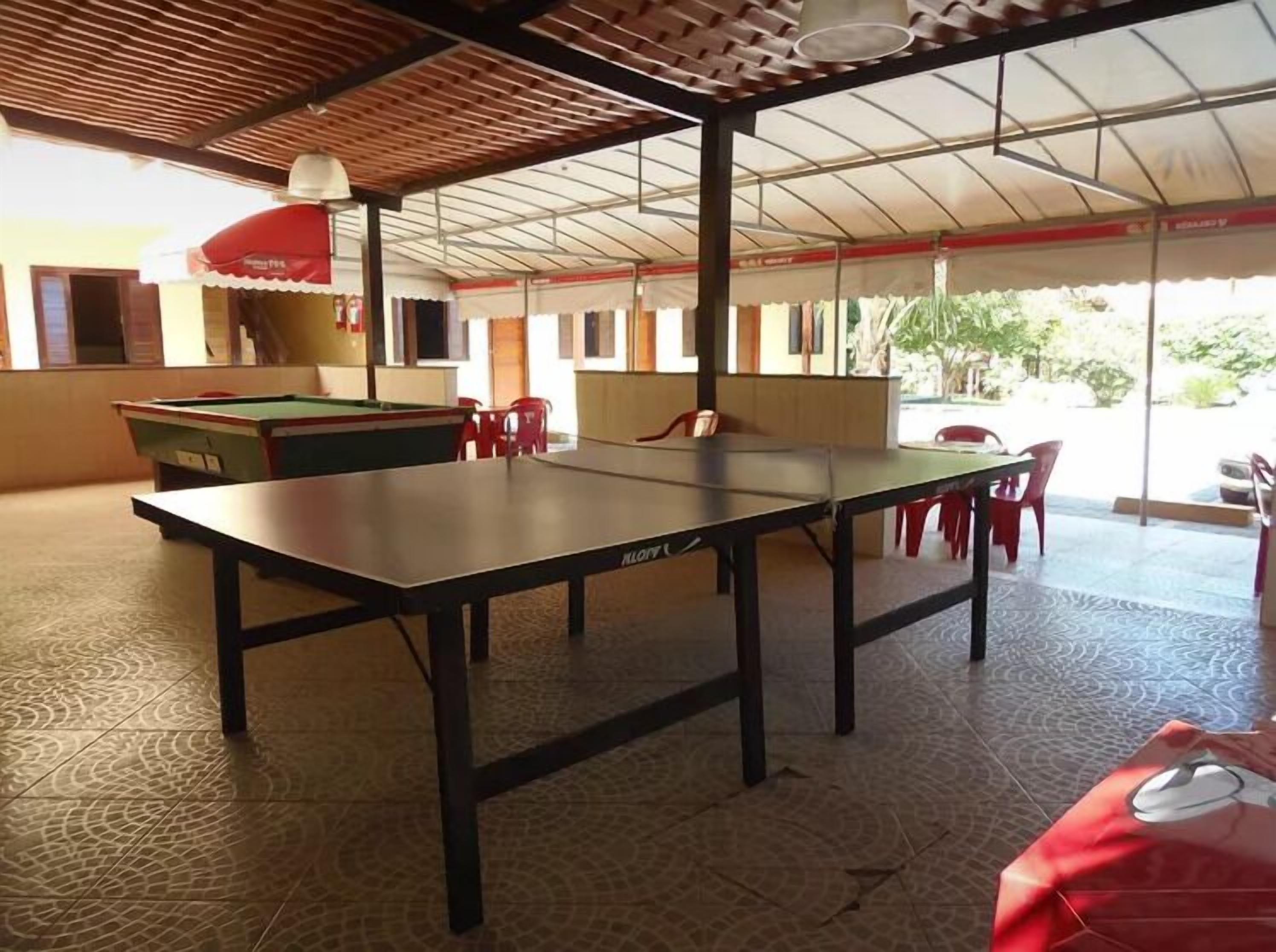 Uma mesa de bilhar numa área coberta, com mesa de sinuca e cadeiras vermelhas.
