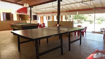 Uma mesa de bilhar numa área coberta, com mesa de sinuca e cadeiras vermelhas.