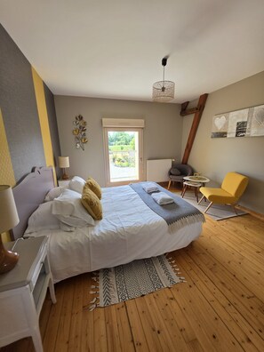 A bedroom with a bed, bedside tables, a chair, a radiator, and a view of greenery outside. - Gîte Mon Pré Vert (Saint-Ellier-du-Maine)