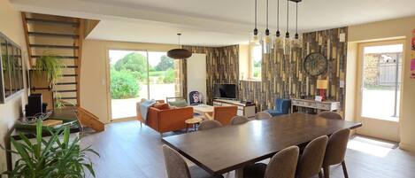 Un amplio espacio de sala con una gran mesa de madera para comer, asientos cómodos y vistas al exterior.