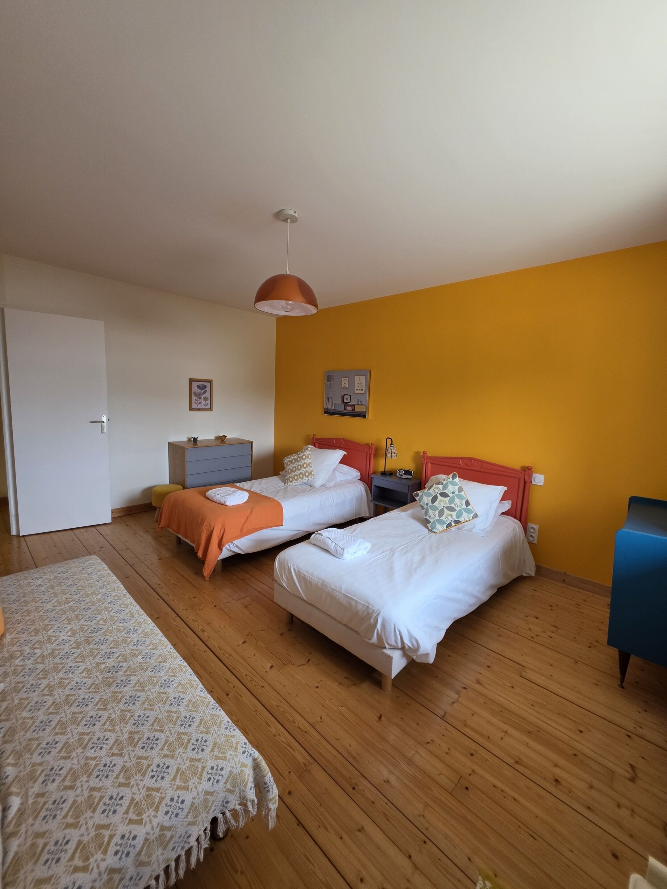 A bedroom with two beds, wooden flooring, a single hanging light fixture, and a wall-mounted power outlet.