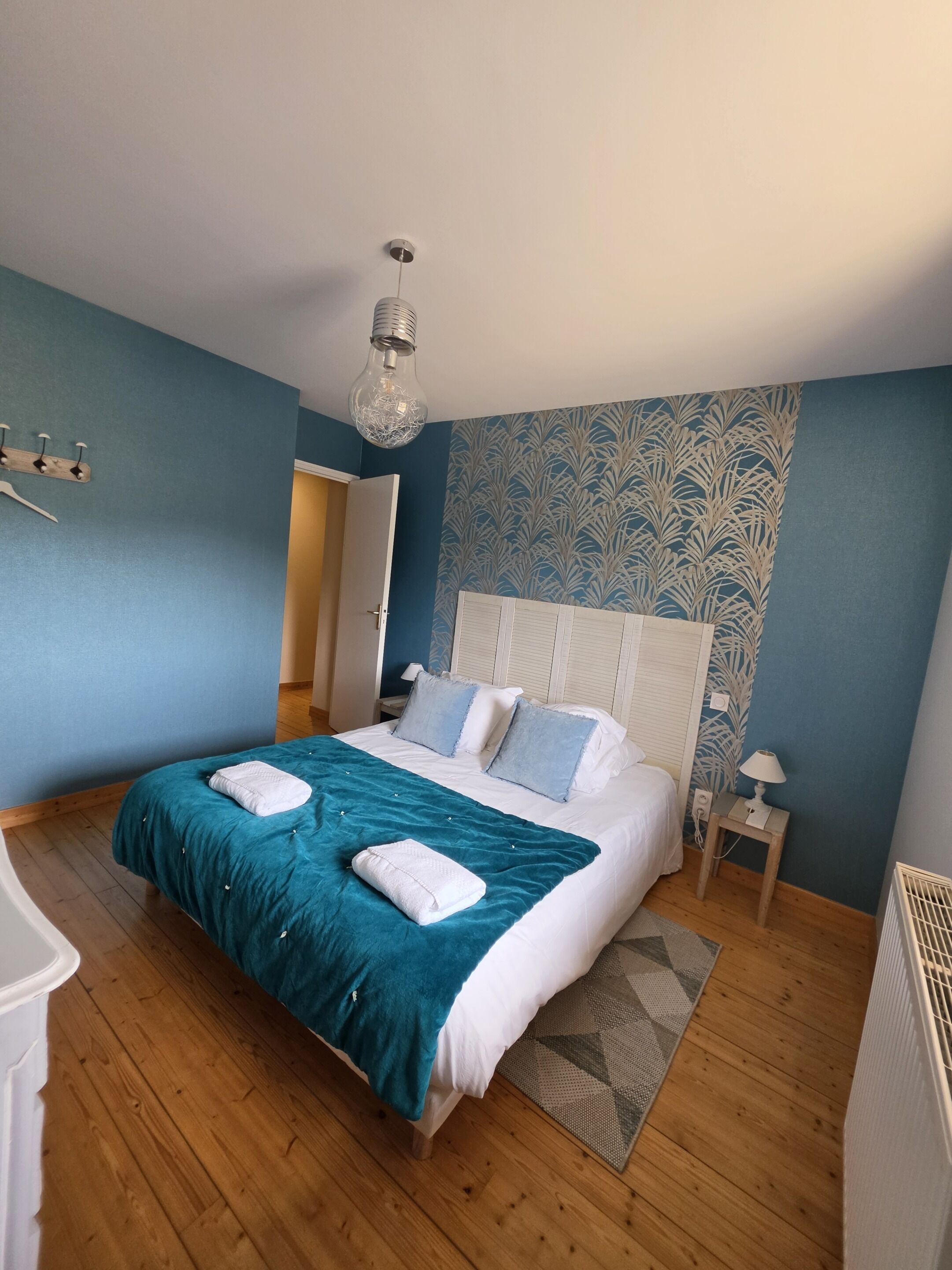 Ein Schlafzimmer mit einem großen Bett, einem Nachttisch, einer Lampe, einer Wandleuchte und einer Tür.