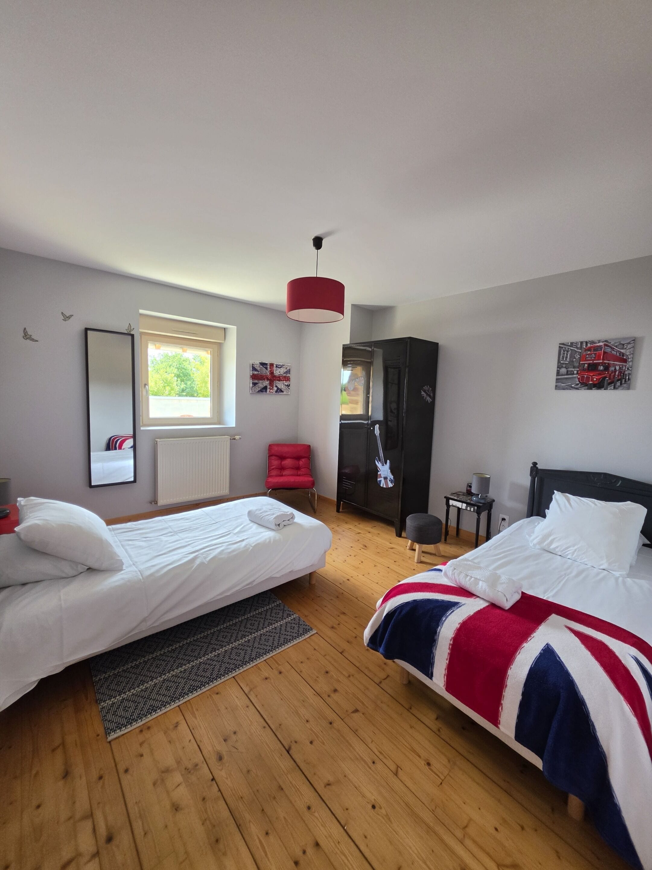 Een slaapkamer met twee bedden, een rode stoel, een kledingkast, een spiegel en een raam.