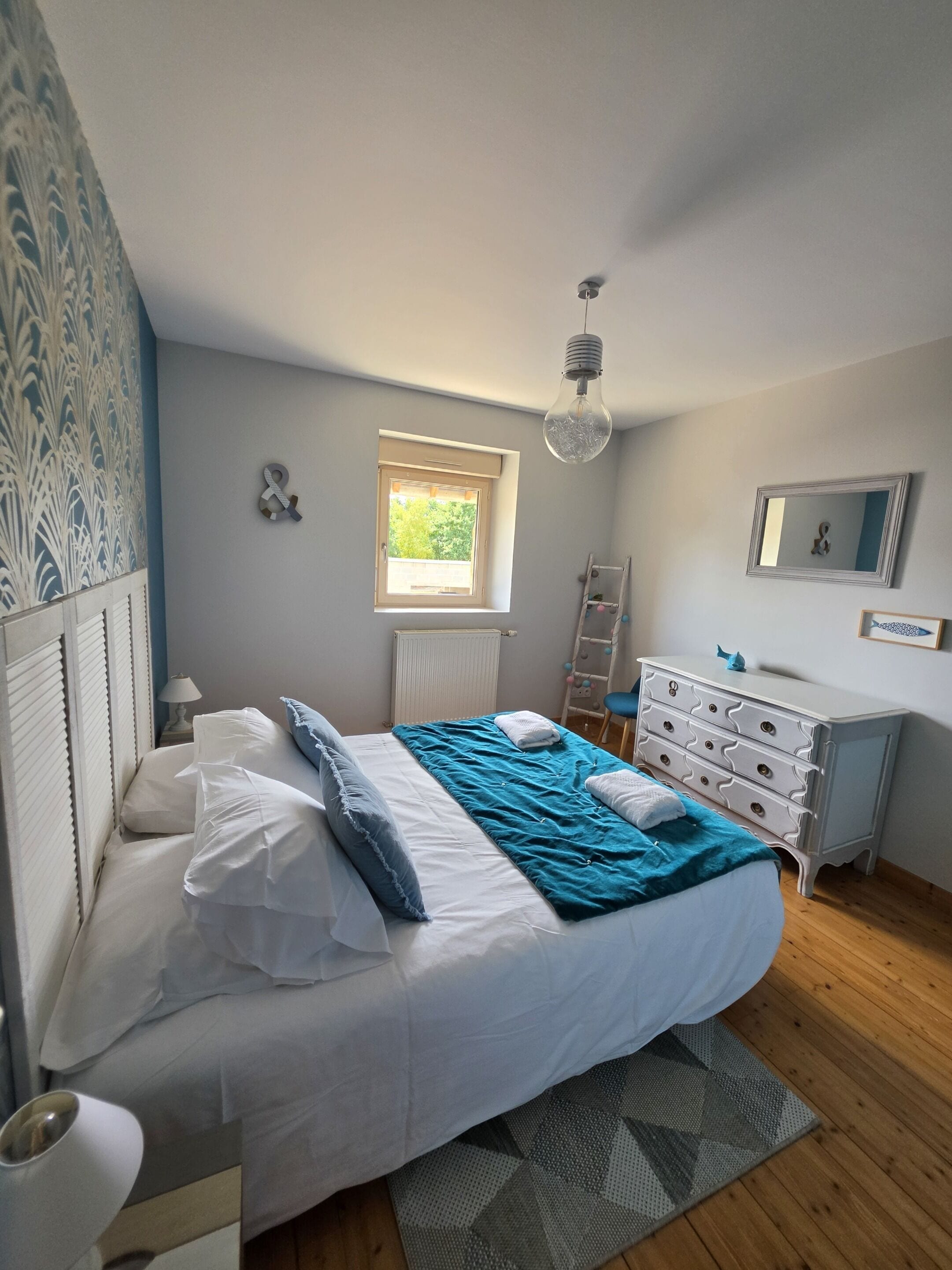 Ein Schlafzimmer mit Bett, Kommode, Fenster und Heizkörper.