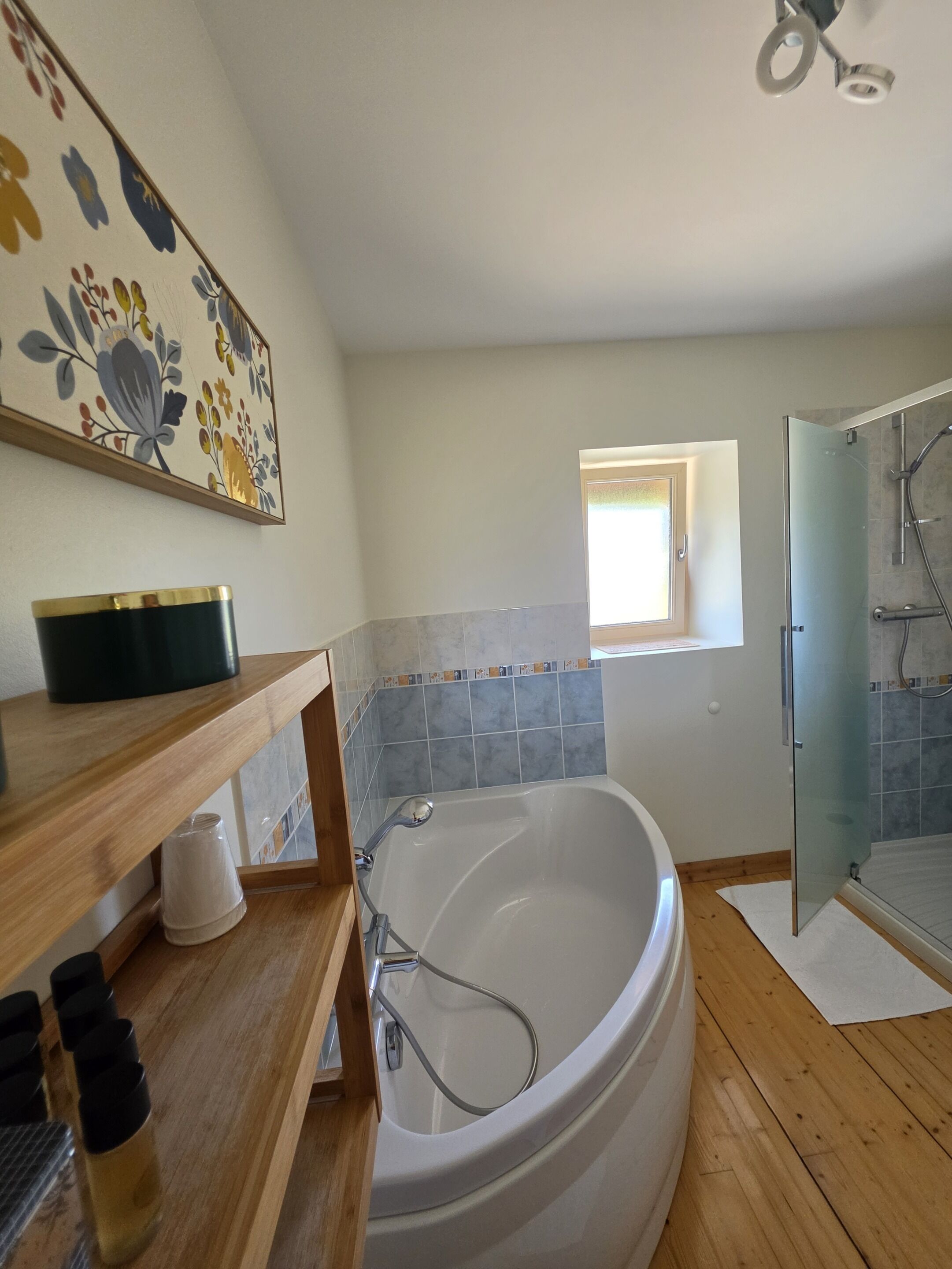 A bathroom with a freestanding bathtub, a glass shower enclosure, a wooden vanity, and a floral artwork on the wall.