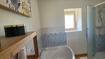 A bathroom with a freestanding bathtub, a glass shower enclosure, a wooden vanity, and a floral artwork on the wall.
