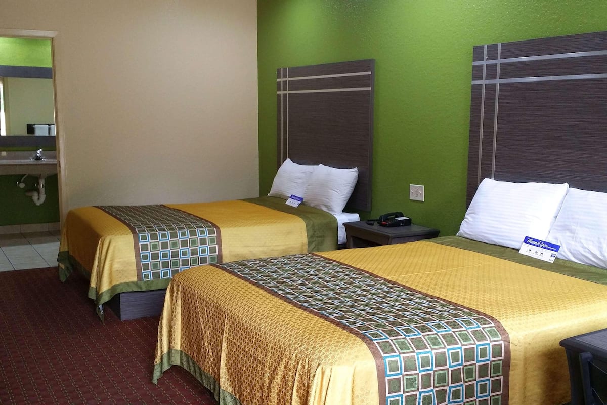 A hotel room with two beds, a nightstand, a mirror, and a sink.