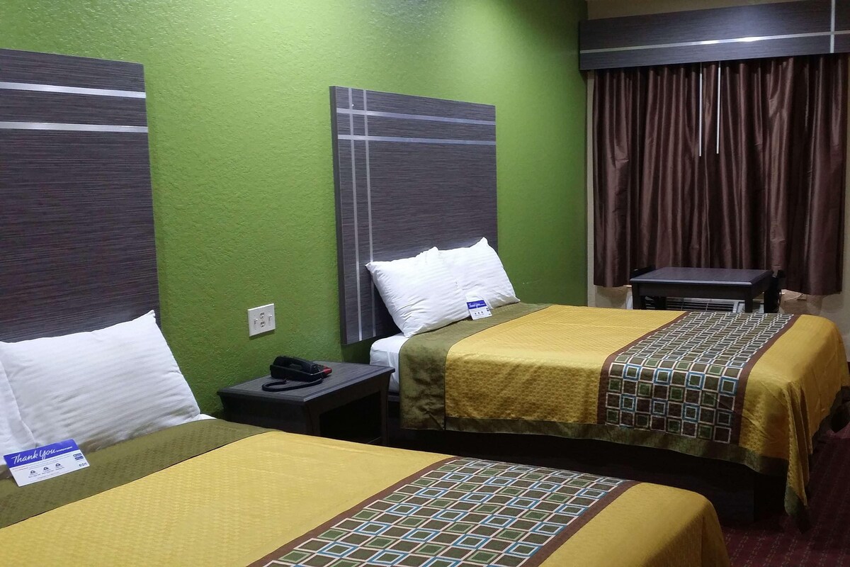 Une chambre d’hôtel avec deux lits, une petite table, une chaise, un rideau et une porte.