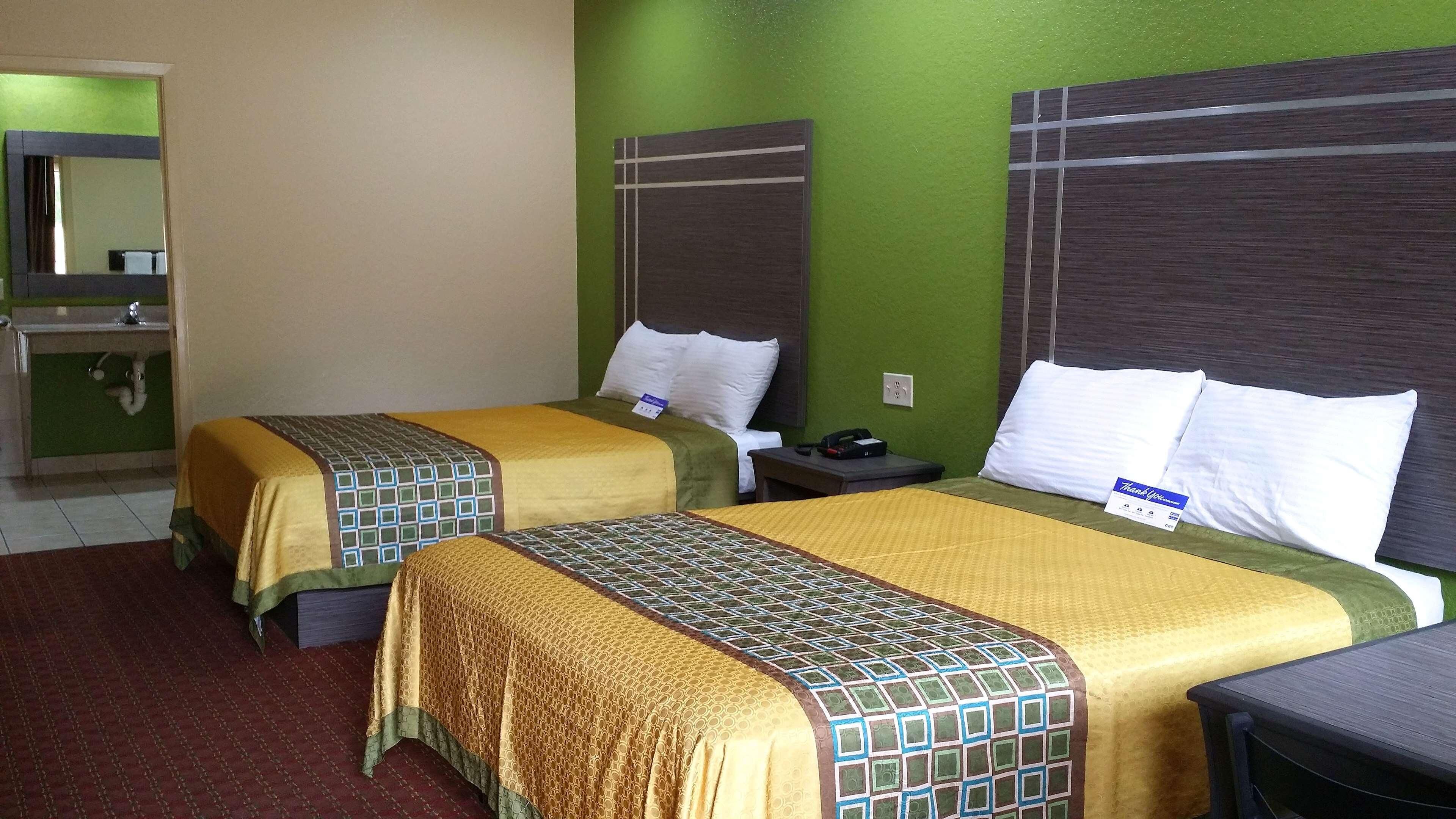 A hotel room with two beds, a nightstand, a mirror, and a sink.