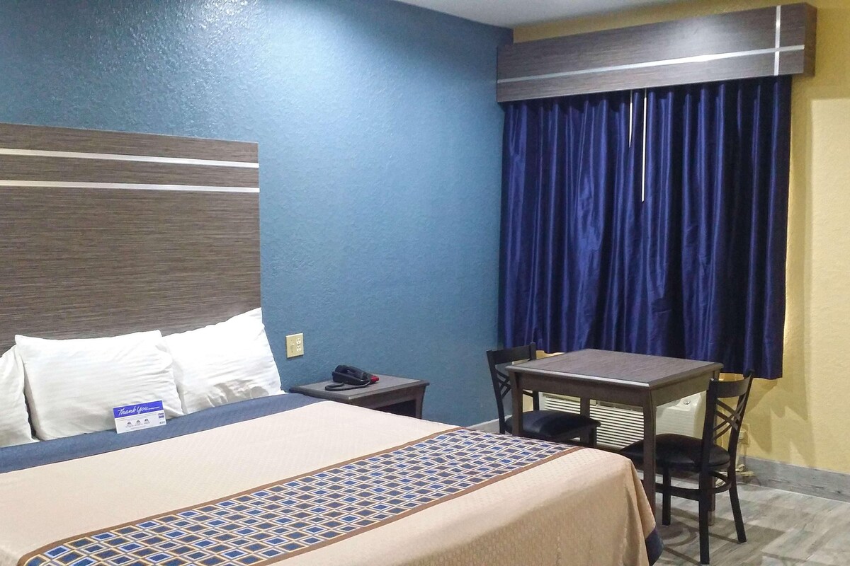 A hotel room with a bed, a desk, a chair, a telephone, and a window with curtains.