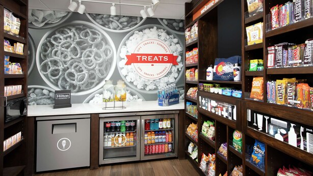 A snack and beverage section with shelves stocked with various snacks and drinks, a refrigerated display case, and a counter with a 'Hilton HONORS' sign. - Hampton Inn Denver Tech Center South CO (Englewood)
