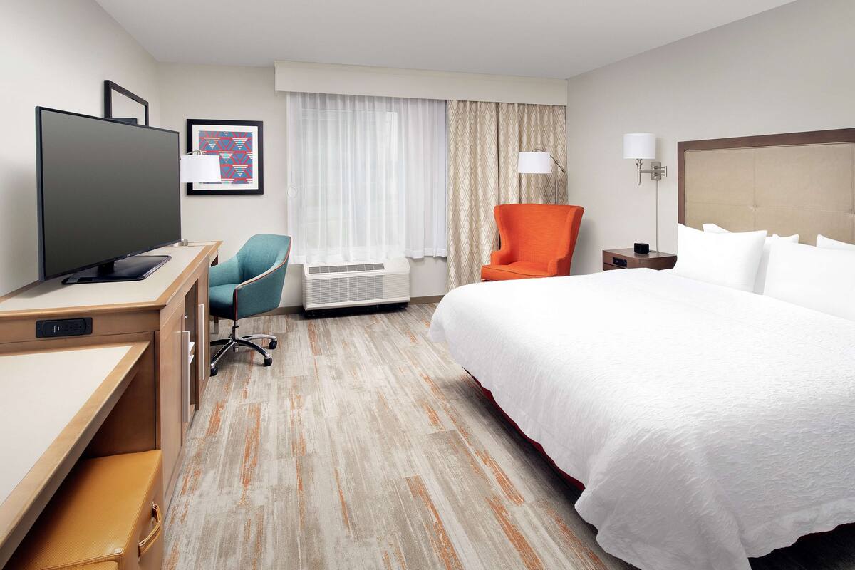 A hotel room with a bed, desk, chair, TV, and a window with curtains.