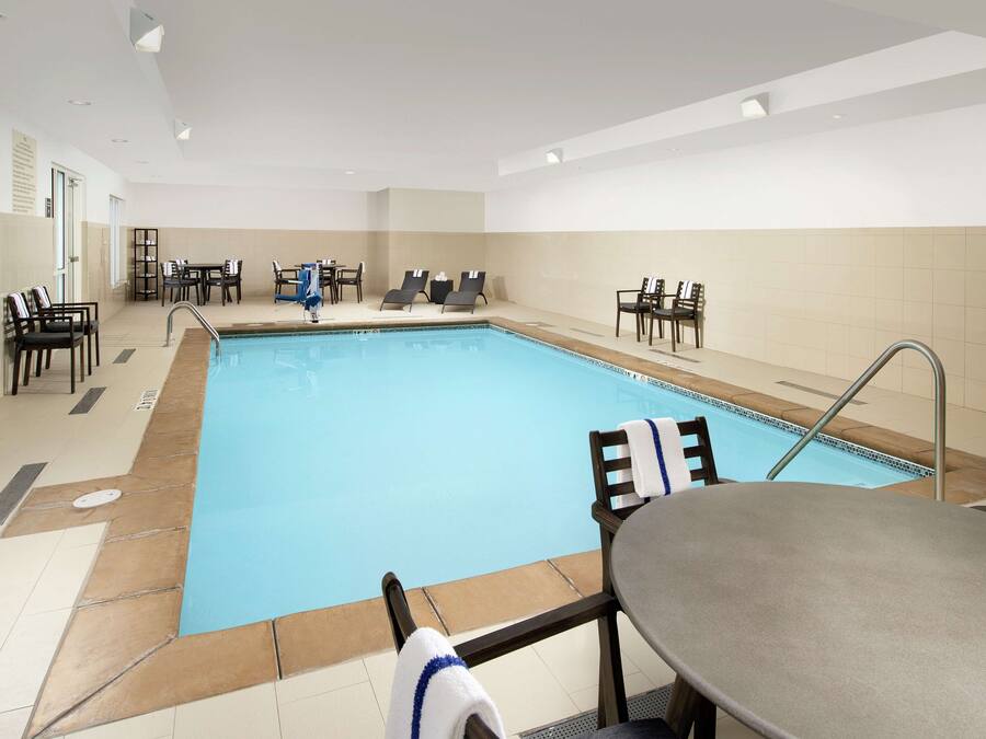 A swimming pool area with lounge chairs and tables, a poolside bar, and a tiled floor.