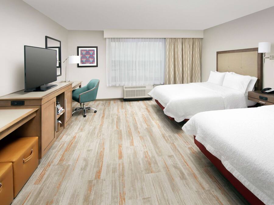 A hotel room with a desk, two beds, a TV, a chair, and a window with curtains.