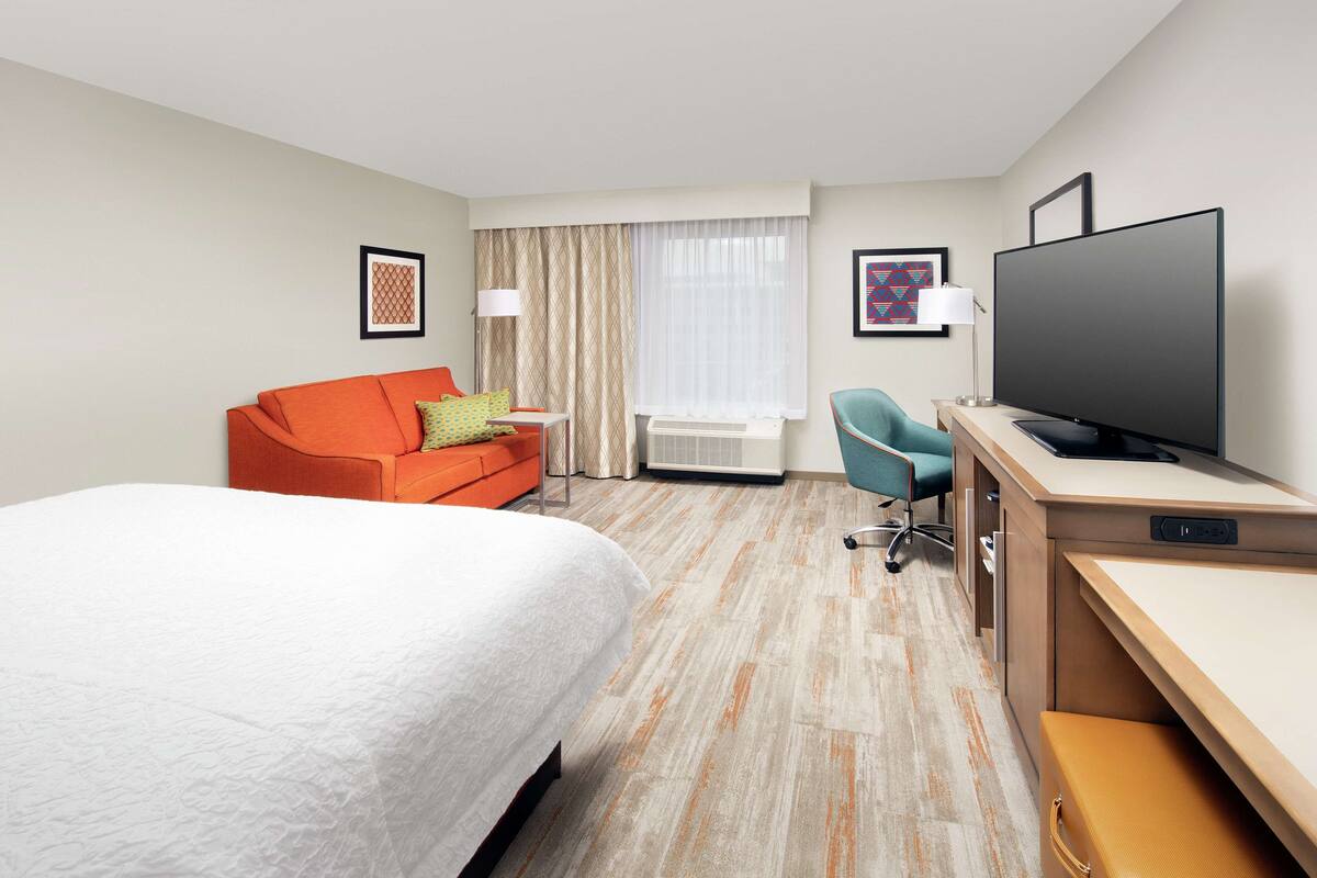 A hotel room with a bed, a desk, a television, a chair, and a window with curtains.