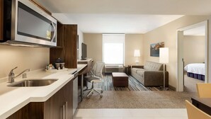 Una habitación de hotel compacta con kitchenette, un sofá, una cama y una ventana.