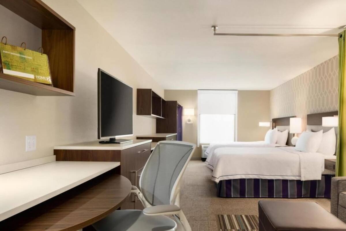 A hotel room with a desk, chair, TV, bed, and bedside table.