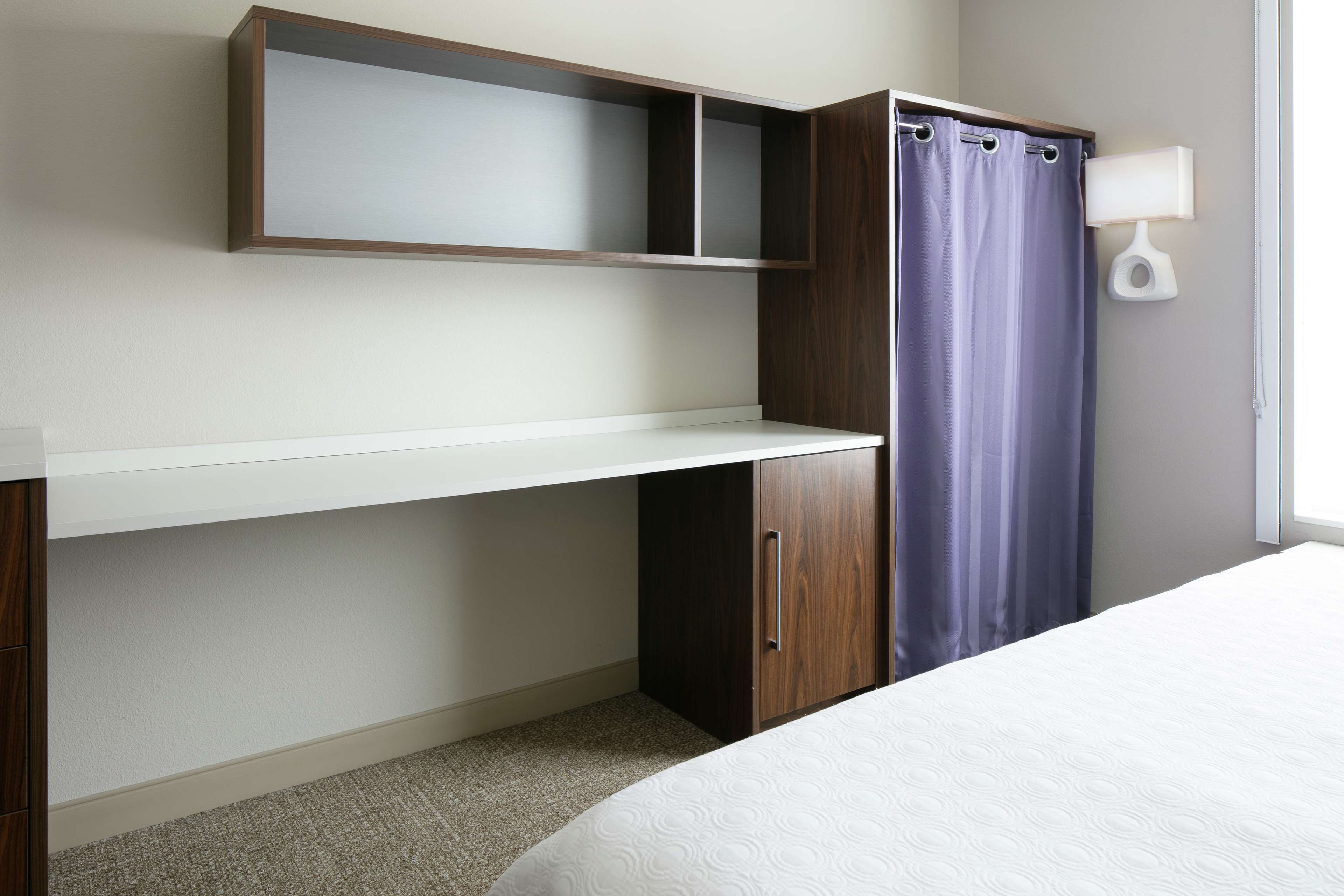 A bedroom with a bed, a desk, a wardrobe, and a window with a curtain.