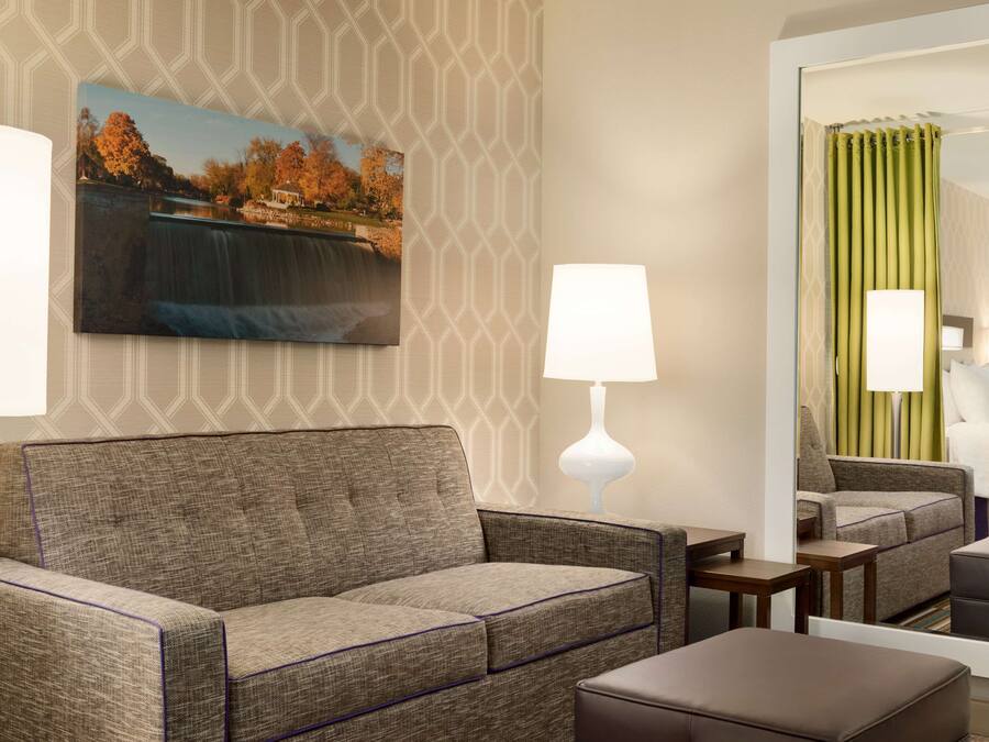 Habitación de hotel con sofá, una mesita, lámpara, un cuadro de una cascada y un espejo que refleja la habitación.